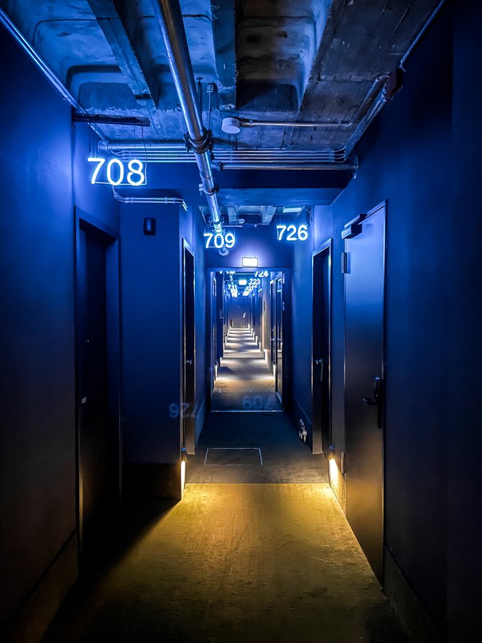 Berlin Nights Photography by Carl Carter capturing a subtly and eerie lit hallway leading to hotel rooms denoted by neon room numbers.