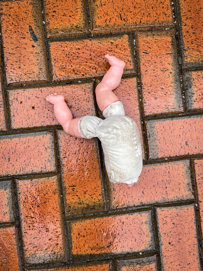 Lost and destroyed - Photography by Carl Carter shows a childs doll with a missing head and clothes, lost and and left on the wet brick floor.